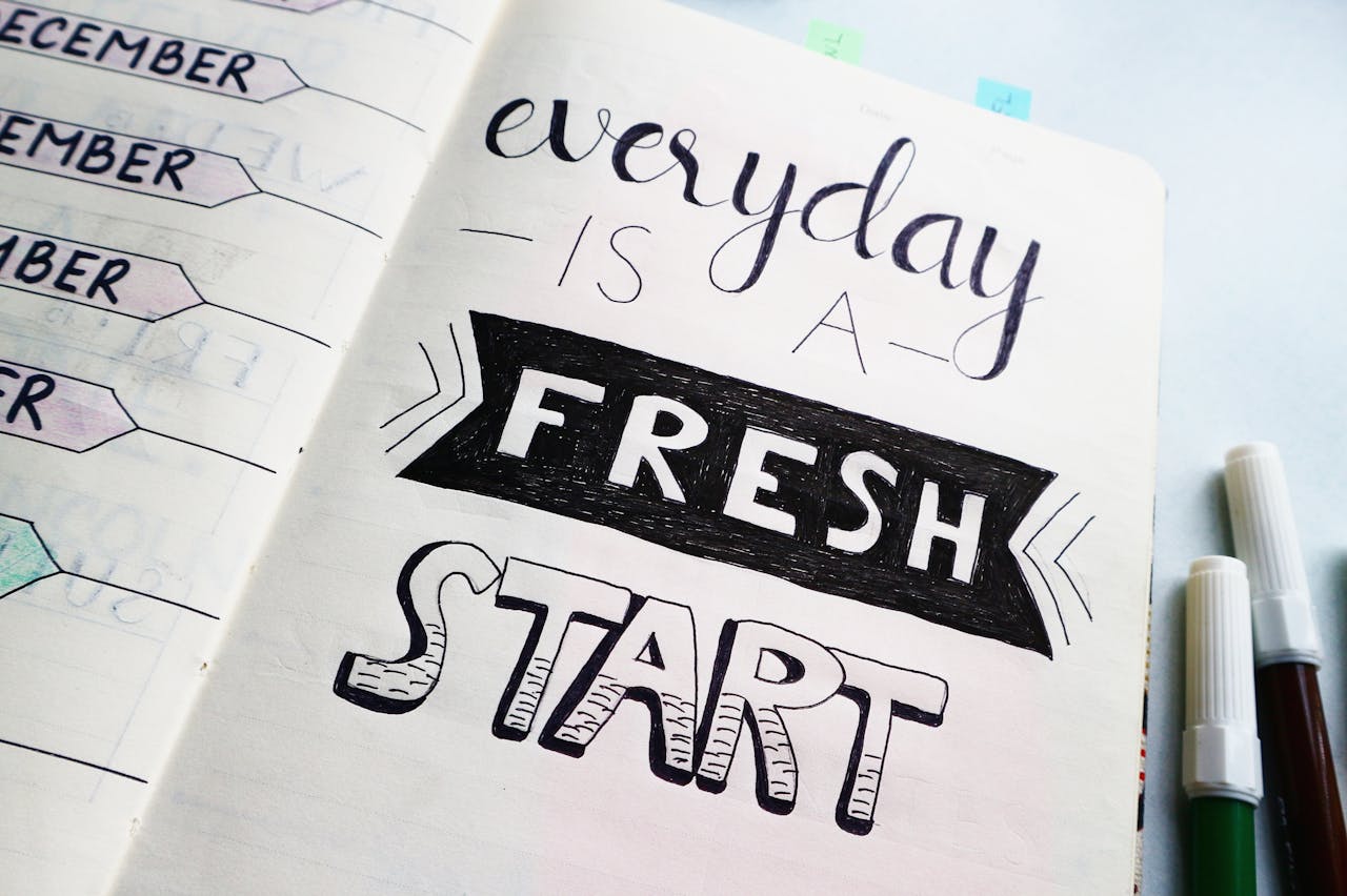 hero-img-02 Notebook page featuring motivational quote 'Everyday is a fresh start' with colorful pens.